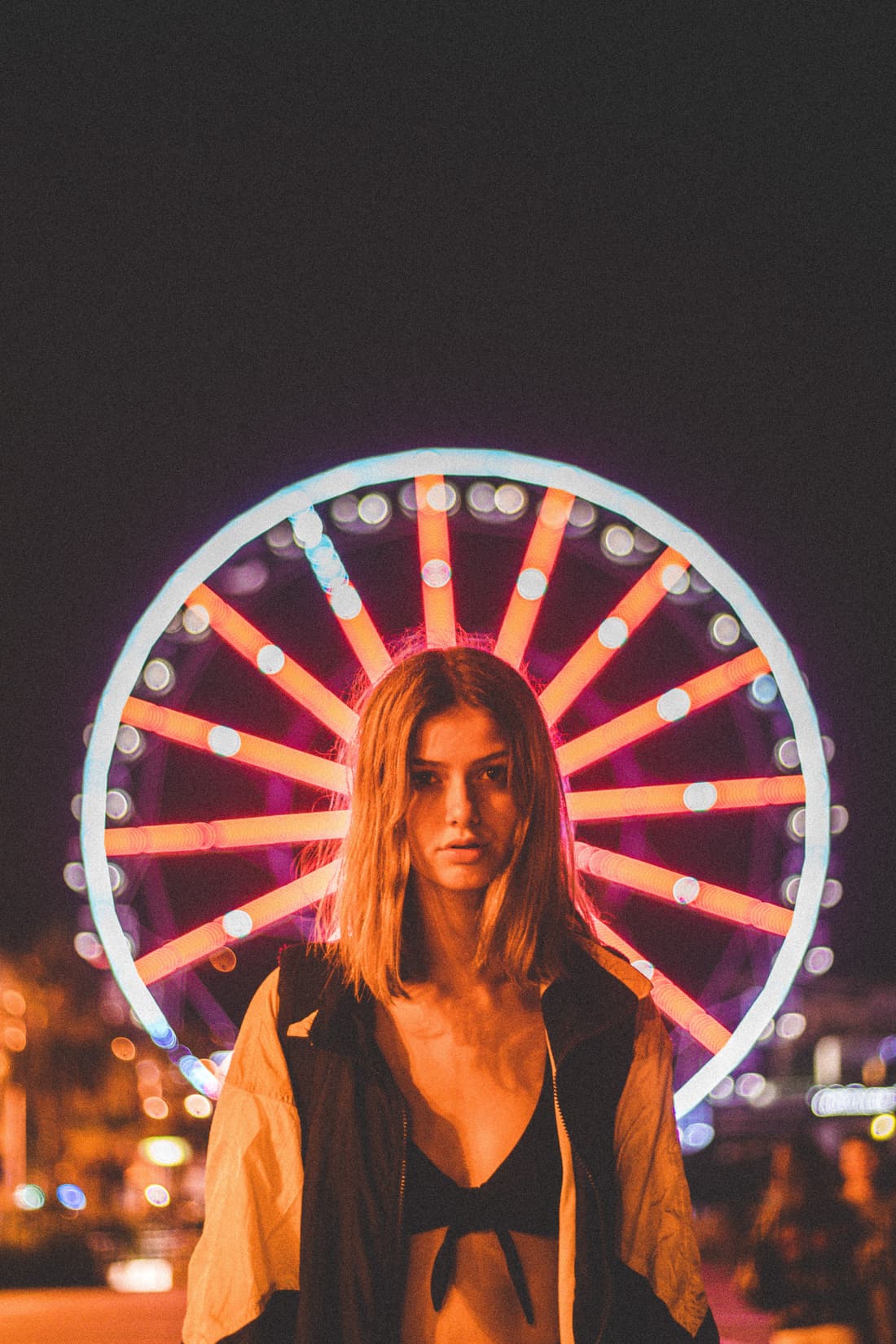 A woman framed by the lights of a Ferris wheel at night