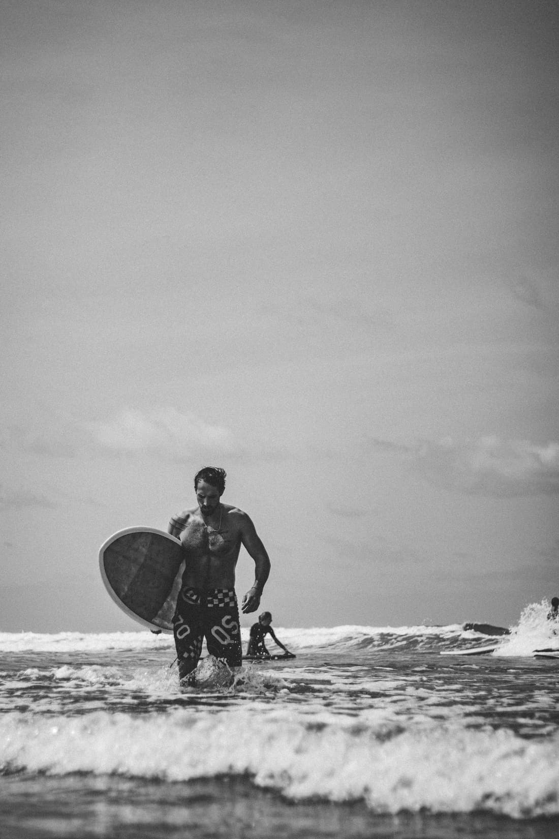 A surfer walking through shallow water in a black and white photograph
